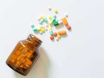 variety of pills spilling out of brown medication bottle